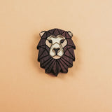 A handcrafted geometric Lion Pin brooch with a dark brown mane and light beige face, displayed on a plain light tan background.
