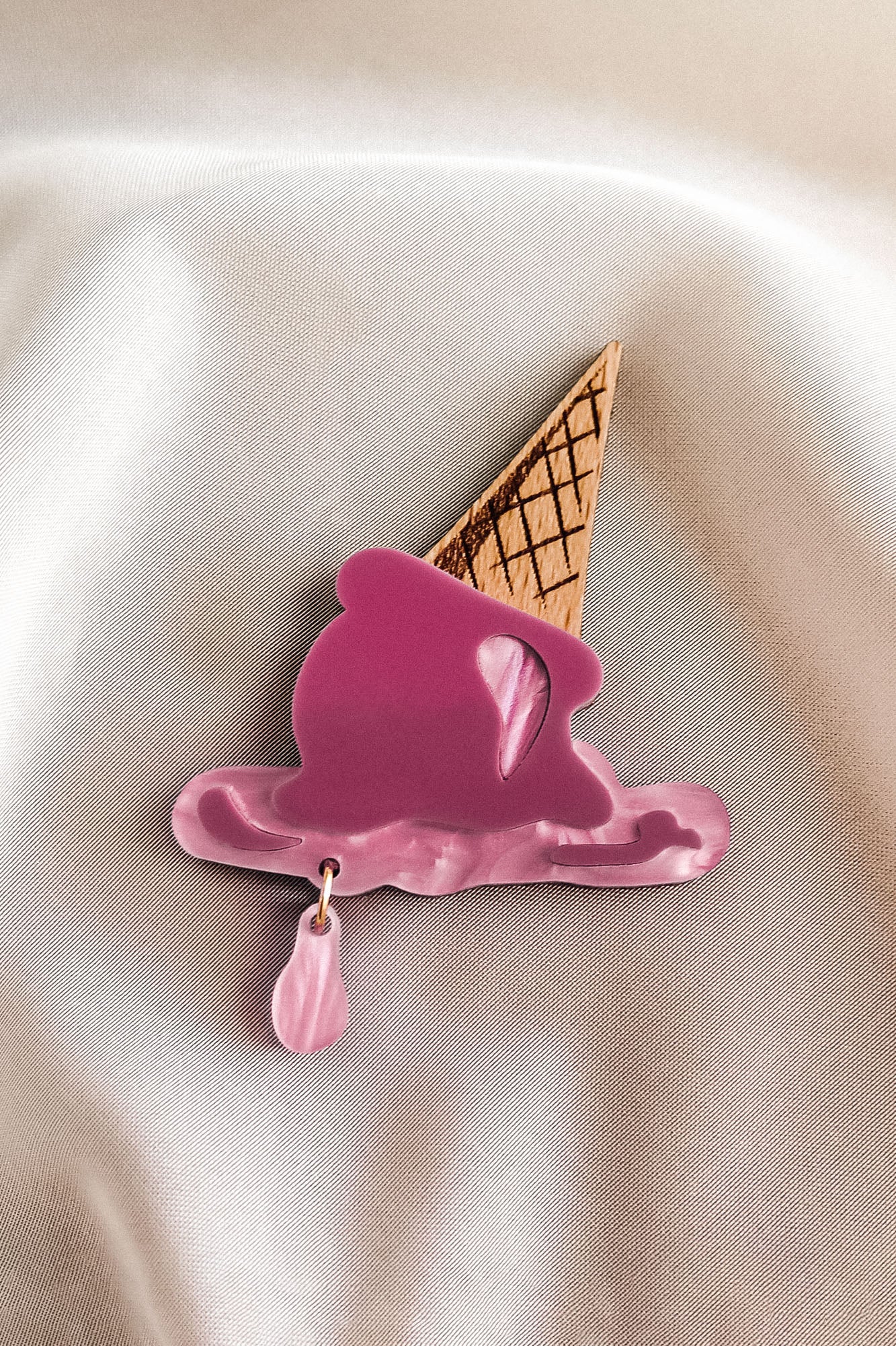 The handcrafted Melted Ice Cream Brooch, shaped like a melting pink cone with a waffle base, lies on soft beige satin—perfect for adding charm to your summer wardrobe.