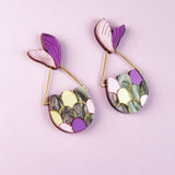 Two colorful Mermaid Tail Earrings with purple, pink, yellow, green, and marbled scales add whimsical elegance—perfect for mermaid lovers—displayed on a light purple background.