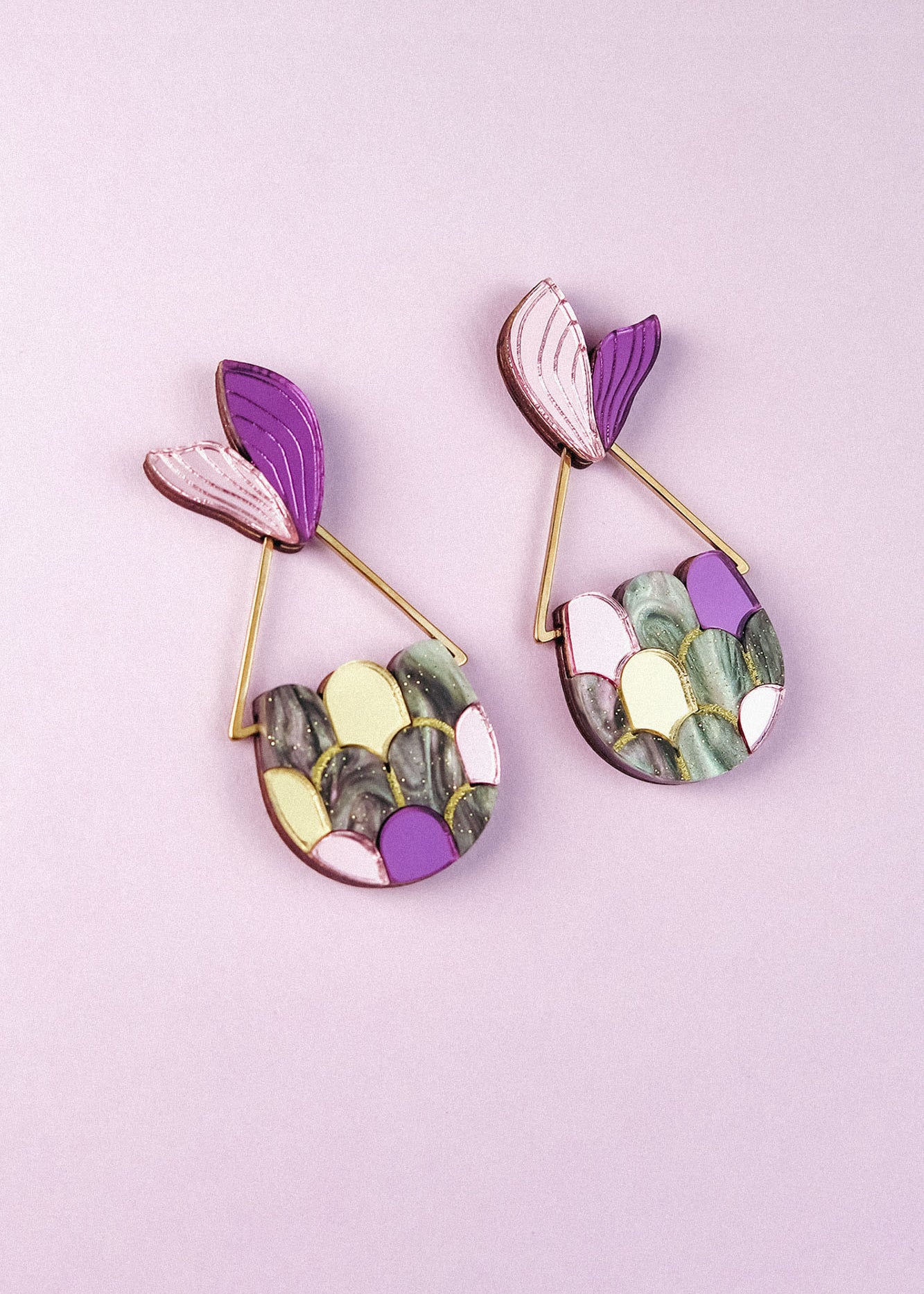 Two colorful Mermaid Tail Earrings with purple, pink, yellow, green, and marbled scales add whimsical elegance—perfect for mermaid lovers—displayed on a light purple background.