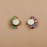 Minimalist Geometric Stud Earrings featuring two semicircular designs with round silver centers: the left earring shows a green and brown marbled pattern, while the right displays pink and purple, set against a plain beige background.