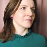 A woman with shoulder-length brown hair wearing a teal top with a ruffled collar and Minimalist Geometric Stud Earrings stands in front of pink curtains, looking slightly to the right with a neutral expression.
