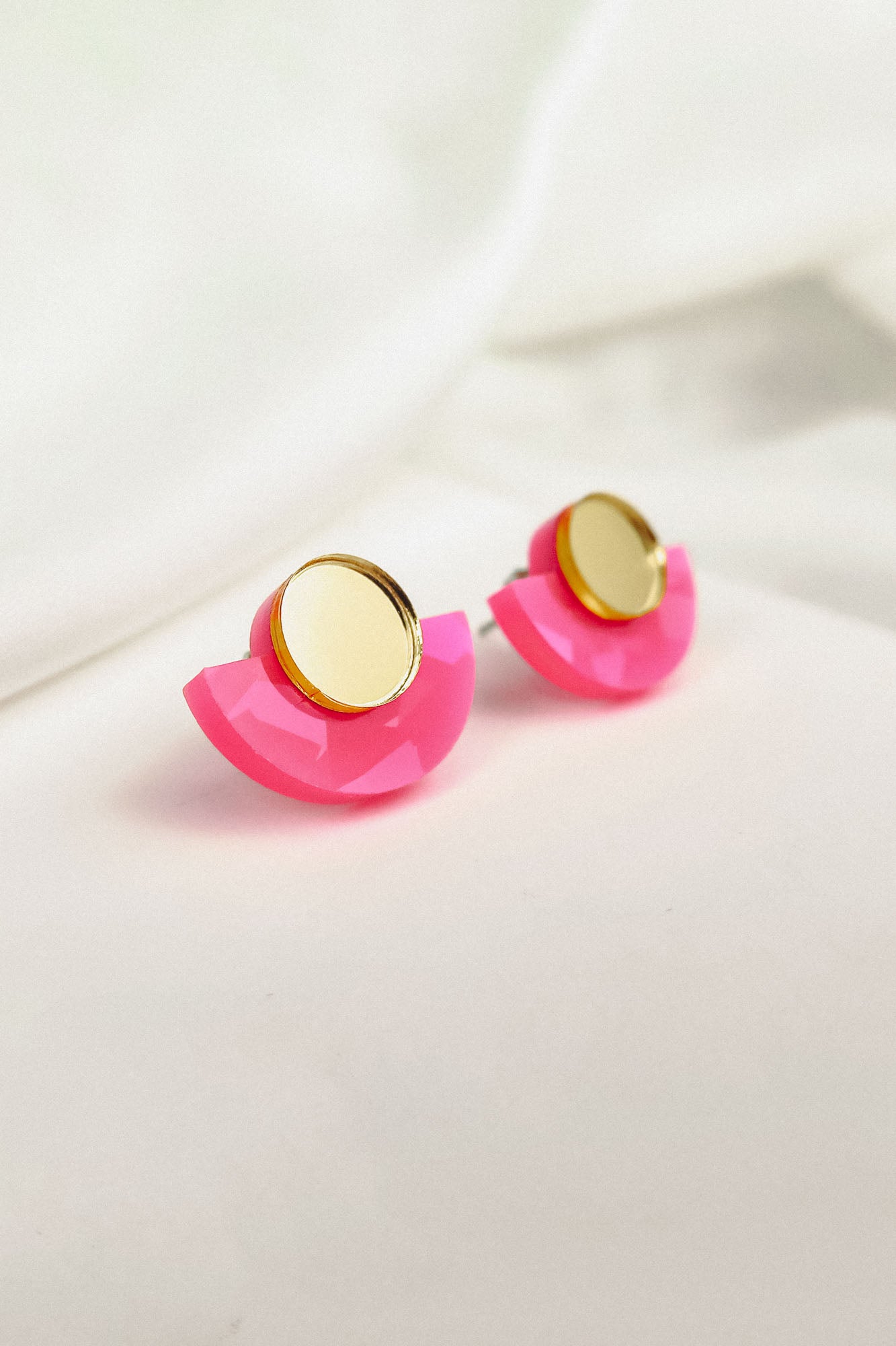 Minimalist Geometric Stud Earrings featuring gold circular tops and bright pink, semi-circular acrylic bases. Lightweight and hypoallergenic, they’re displayed on a soft white surface for a modern, stylish touch.