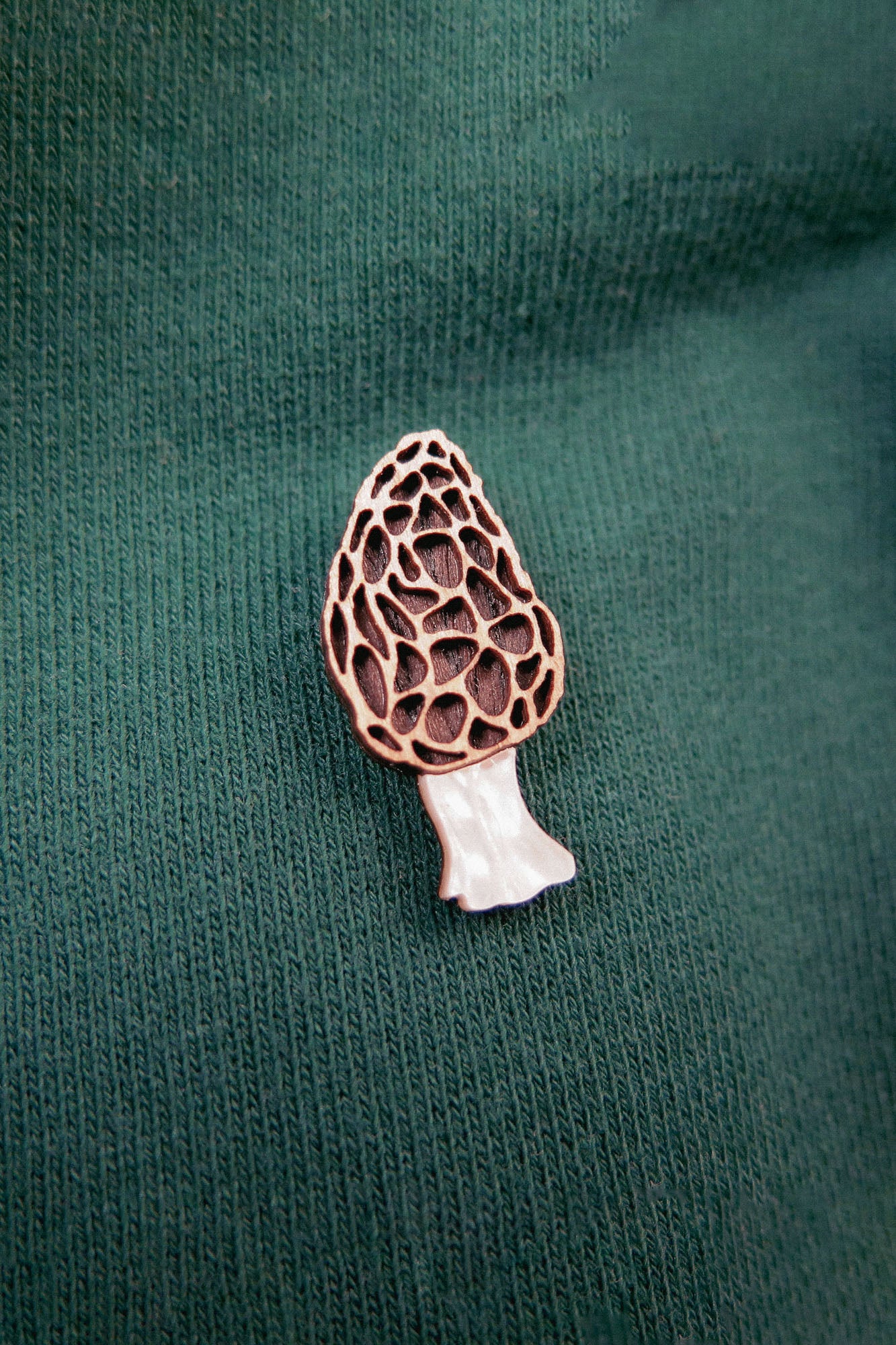 A handcrafted Morel Mushroom Pin is attached to a green, ribbed fabric, likely on a shirt or sweater.