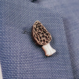 A close-up of a blue textured blazer with a handcrafted Morel Mushroom Pin, made from eco-friendly materials, attached to its lapel.