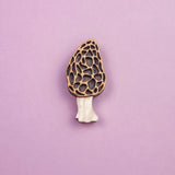 A handcrafted Morel Mushroom Pin made from eco-friendly materials features a textured, honeycomb-patterned cap and pale stem, displayed on a light purple background.