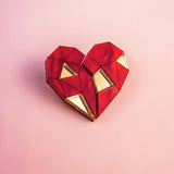 A geometric, origami-style red heart with gold triangular accents sits on a soft pink background—perfect as romantic gift or inspiration for handcrafted pins.