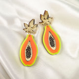 Add a playful pop to your look with these Papaya Earrings, crafted from neon acrylic glass and featuring allergy-free stainless steel hooks. The colorful halves with gold leaves and black seeds are displayed on smooth white satin fabric.