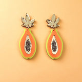 Papaya Earrings made of allergy-free stainless steel and neon acrylic glass, featuring orange with green edges, black seed details, and silver leaves, all set against a peach-colored background.