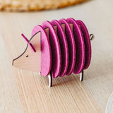 A small, decorative, pink and wood-colored armadillo figurine with a segmented, accordion-like body stands on a light wooden surface—perfect as a quirky housewarming gift.