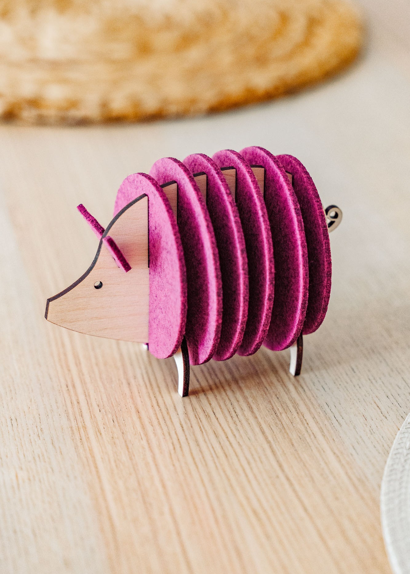 A small, decorative, pink and wood-colored armadillo figurine with a segmented, accordion-like body stands on a light wooden surface—perfect as a quirky housewarming gift.