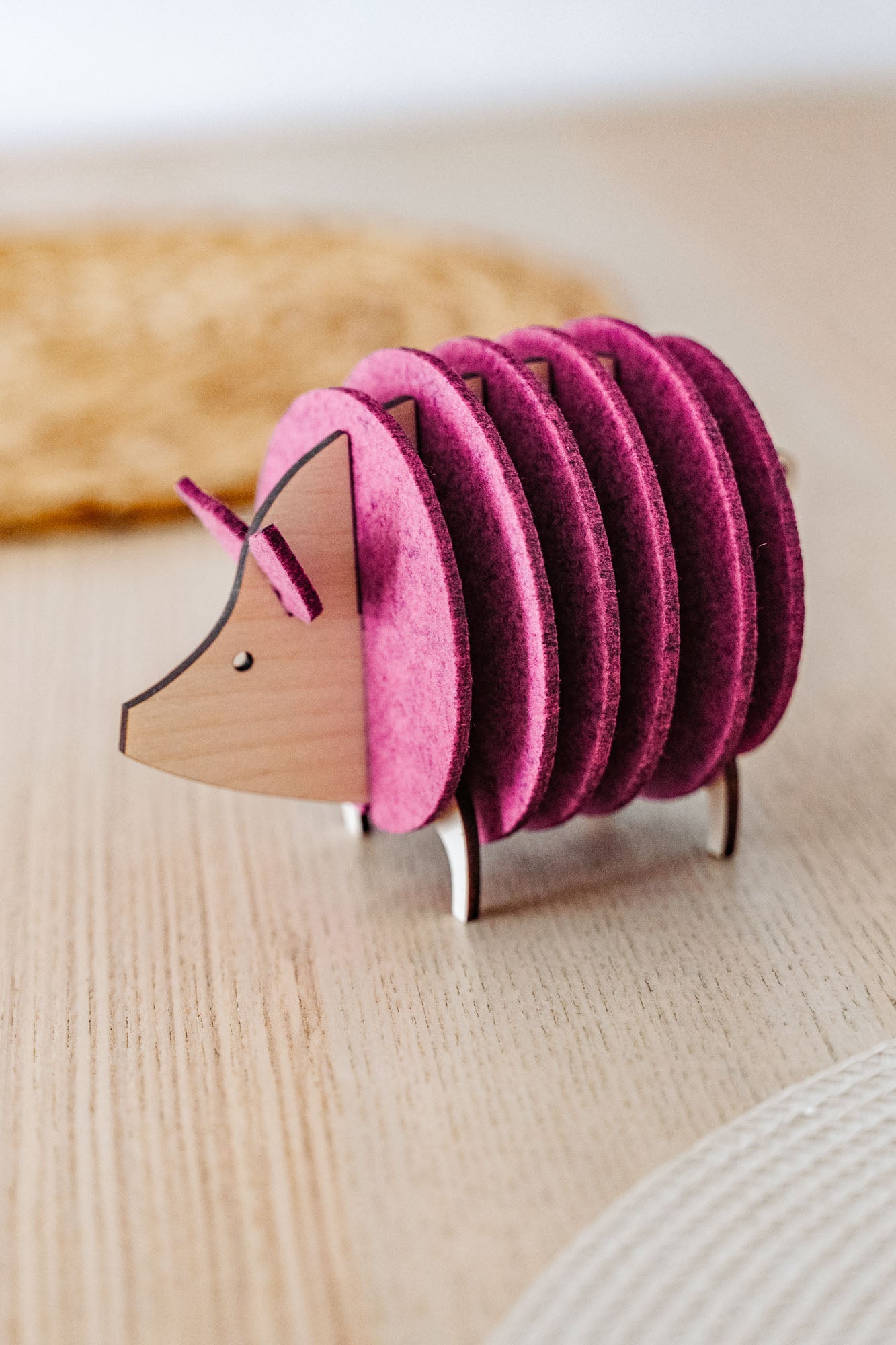 A wooden and felt coaster holder shaped like a hedgehog, with pink felt discs forming the body, sits on a light wooden table—a charming housewarming gift for any home.