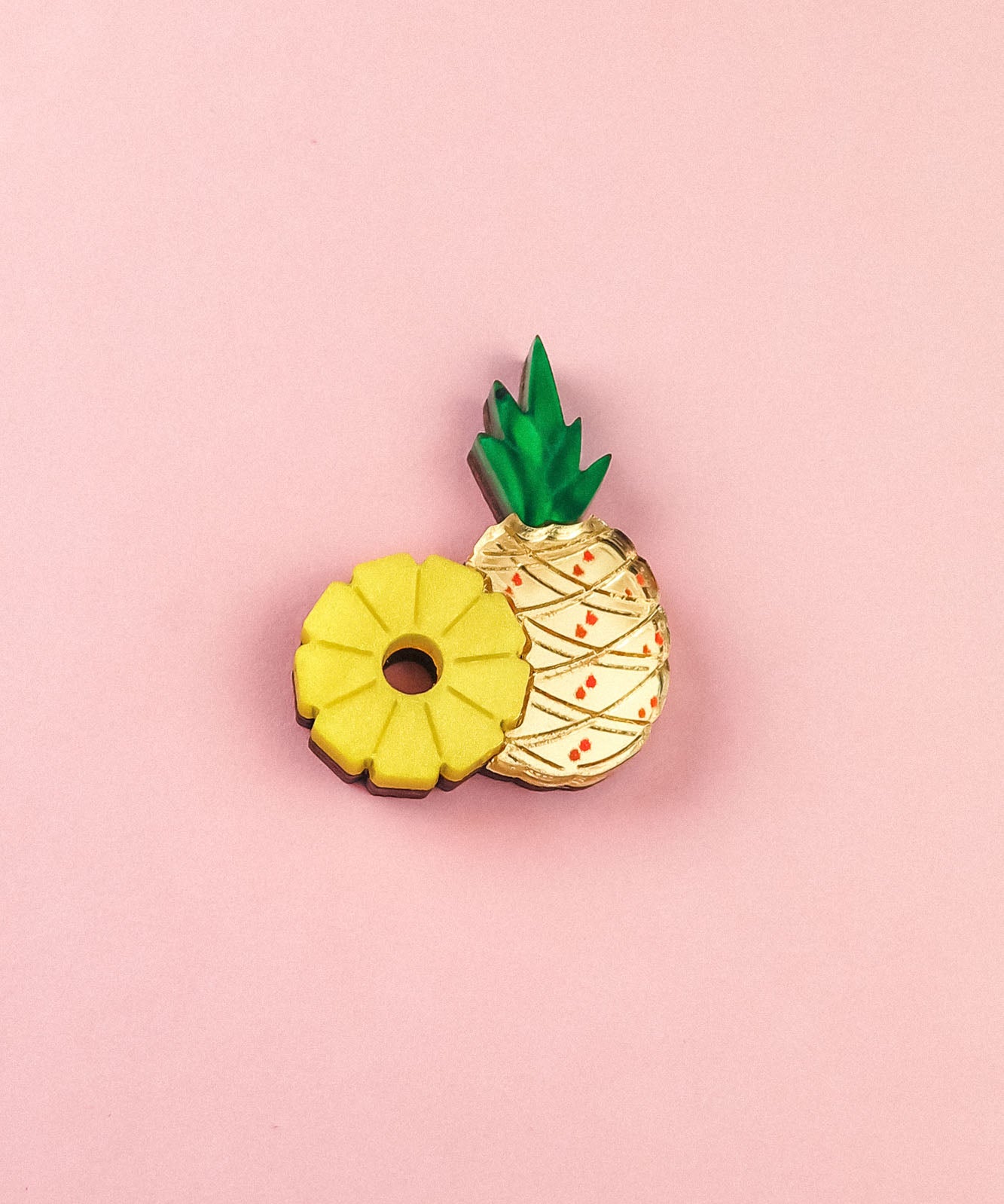 Two cookies on a pink background: one is handcrafted and shaped like a yellow pineapple ring, while the other resembles a whole pineapple with green leaves and a textured cream-colored surface—resembling a sweet Pineapple Pin accessory.