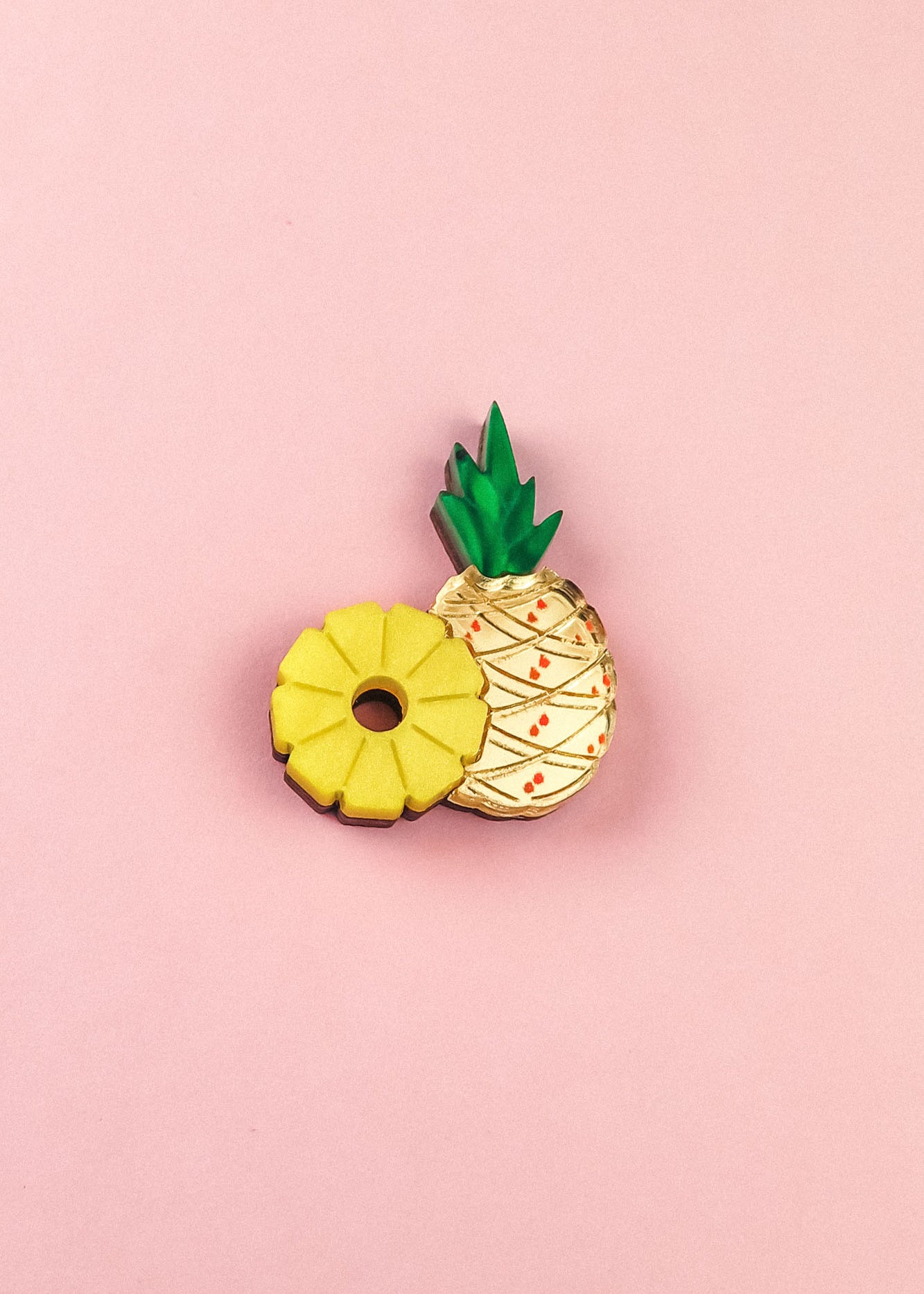 Two cookies on a pink background: one is handcrafted and shaped like a yellow pineapple ring, while the other resembles a whole pineapple with green leaves and a textured cream-colored surface—resembling a sweet Pineapple Pin accessory.
