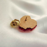 A handmade wooden pin shaped like a heart with a gold butterfly clutch backing rests on white satin fabric. Perfect for fashion enthusiasts, this piece features a red edge reminiscent of a Red Poppy Flower Lapel Pin.