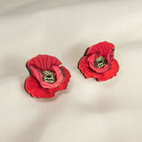 A pair of red, poppy design acrylic earrings with black and green centers, displayed on a soft, light-colored fabric background. Lightweight and eye-catching for any occasion.