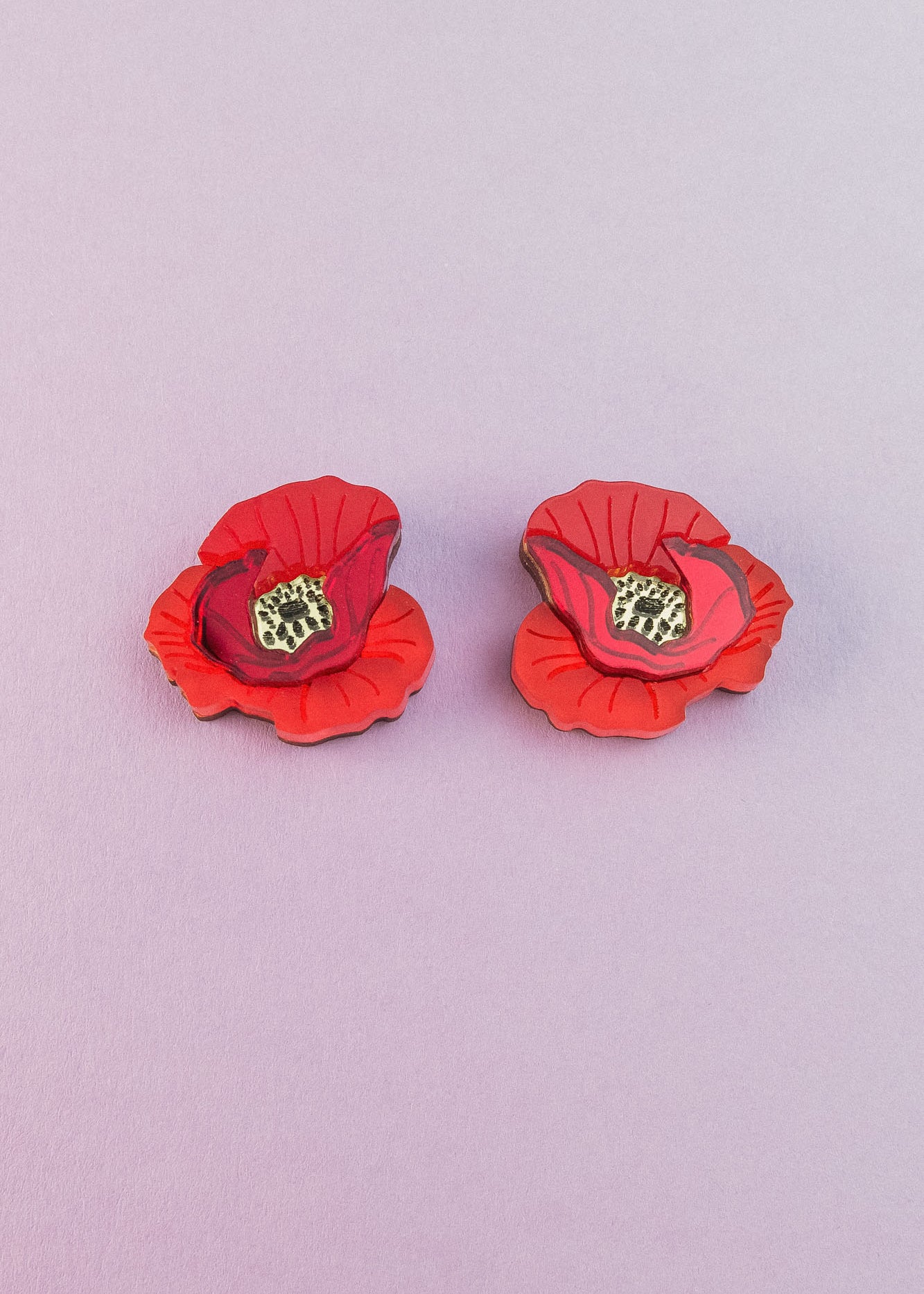 Two lightweight acrylic earrings featuring a vibrant poppy design with black and yellow centers are displayed on a light purple background.