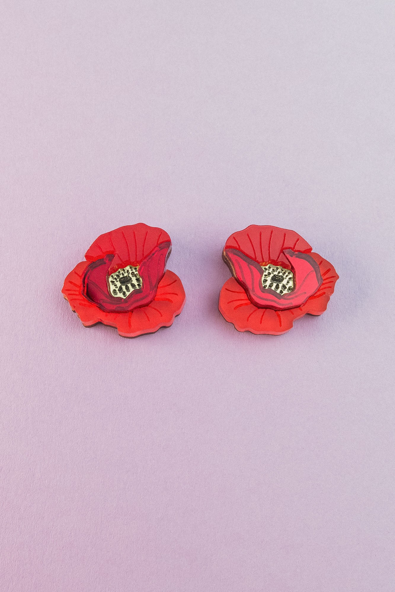 Two lightweight acrylic earrings featuring a vibrant poppy design with black and yellow centers are displayed on a light purple background.
