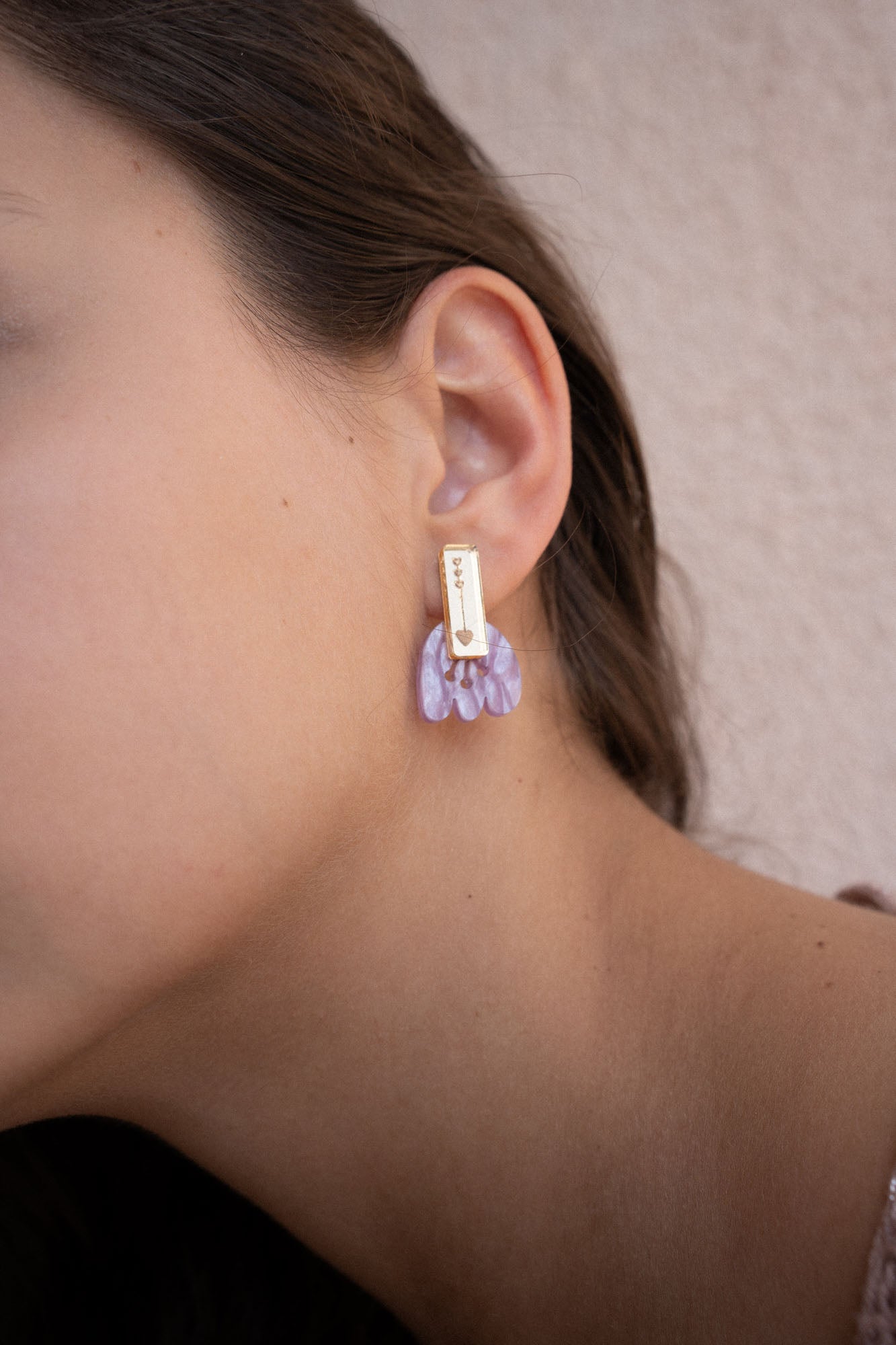 Close-up of a person wearing a gold rectangular earring with marbled purple acrylic petal-shaped accents, against a light beige background. Showcased on the left ear, these Romantic Tulip Earrings offer allergy-free comfort.