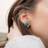 A close-up of a persons ear wearing gold and turquoise Sea Turtle Studs, with their light brown hair partially visible, captures an ocean-inspired, summery vibe.