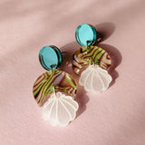 A pair of handmade Seashell Earrings with turquoise circular studs, marbled green and brown semicircle pieces, and translucent white shell-shaped danglers, displayed on a pink textured surface. Lightweight and perfect for any occasion.