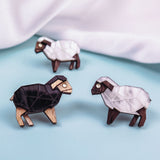 Four geometric wooden sheep figurines, three white and one black, are arranged on a light blue surface with a white fabric backdrop. Their polygonal shapes and minimalist design echo the style of Polygon Sheep Stud Earrings.