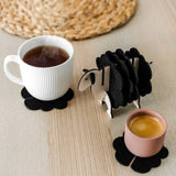 A white mug and a pink cup sit on black felt coasters next to a wooden sheep-shaped coaster holder on a light wooden table with a woven placemat in the background, perfect for charming home decor.