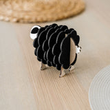 A small, black and white wooden sheep-shaped figure sits on a light wooden table near woven placemats, adding a charming touch to your home decor.