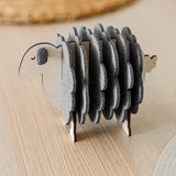 A wooden sheep-shaped coaster holder with round, gray felt coasters arranged to resemble the sheep’s wool stands on a light wooden table—perfect for charming home decor.