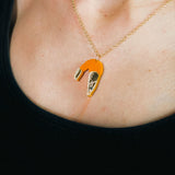 A whimsical Shrimp Pendant Necklace with a gold chain features an orange shrimp charm, playfully displayed above a black top on the wearer’s neck.