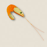A Shrimp Pin accessory designed to resemble a shrimp, with an orange segmented body and detailed gold head, featuring green and black accent stones and long, thin orange antennae—perfect for adding wardrobe charm against any outfit.