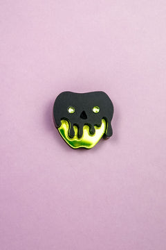 A pin shaped like an apple with a shiny yellow bottom and a black, drippy skull design on top, this Poisoned Apple Badge is perfect for Halloween lovers. Set against a plain light purple background—grab yours now, as stock is limited!.