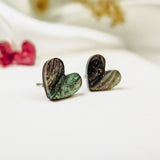 Two Tiny Heart Studs with a marbled green and black pattern are displayed on a white surface, exuding minimalist charm. Perfect for sensitive ears, these hypoallergenic earrings add a subtle touch of style amid softly blurred decor.