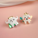 Two cute enamel pins shaped like smiling cartoon teeth, each a handcrafted accessory and true tooth king pin. One wears green wings, the other blue and gold with rosy cheeks, both crowned in gold against a soft pink background.
