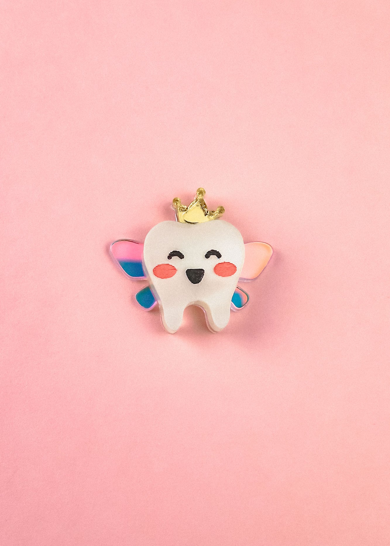 A smiling cartoon tooth with rosy cheeks, wings, and a gold crown sits centered on a pink background, making this handcrafted Tooth Fairy Pin perfect for celebrating childhood milestones.