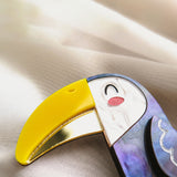 A close-up of a handcrafted Toucan Brooch with a yellow beak, white face, and vibrant painted details, resting on a soft, light-colored fabric background, radiating tropical charm.