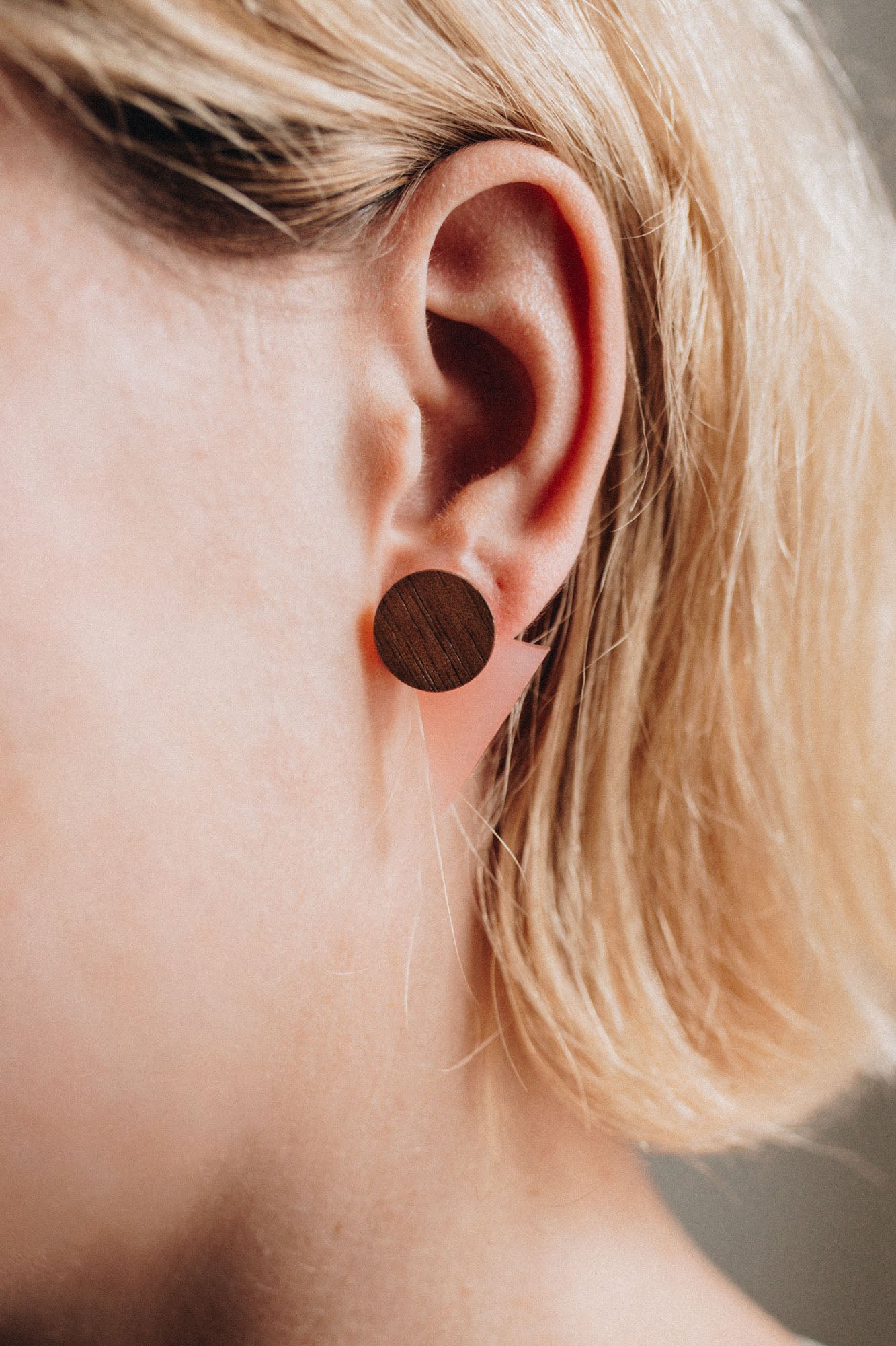 Close-up of a person with short, blonde hair wearing a large, round, handcrafted wooden stud earring in their ear. The focus is on the ear and earring, perfect for elevating any contemporary capsule wardrobe.