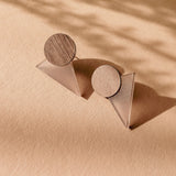 A pair of modern, handcrafted earrings featuring wooden circular tops and translucent triangular bases, displayed on a textured beige surface with soft shadows—perfect for a contemporary capsule wardrobe.