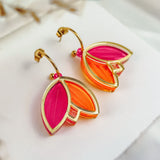 A pair of earrings with gold outlines, shaped like overlapping leaves in vibrant pink and orange colors, showcase artisan craftsmanship. Displayed on a white card with a soft, neutral background, these Tulip Huggie Earrings truly stand out.
