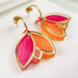 A pair of Tulip Huggie Earrings with artisan craftsmanship, featuring three leaf-shaped charms in vibrant colors—translucent pink and orange outlined in gold—displayed on a white surface.