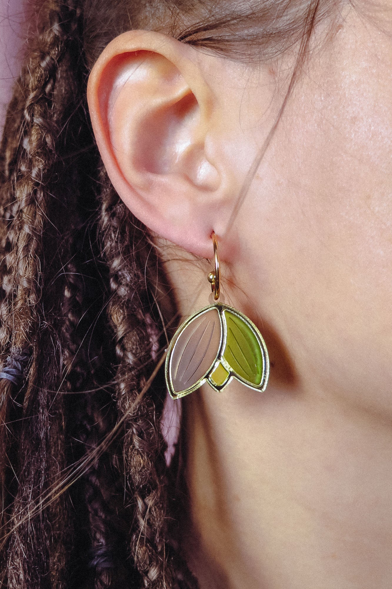 Close-up of a person’s ear with braided hair, wearing lightweight, handcrafted earrings shaped like overlapping leaf segments in brown and green tones with a gold outline.