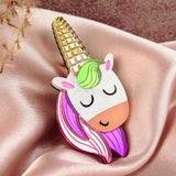A cute handcrafted UniCorn Brooch with a gold horn, green mane, pink-and-purple hair, and closed eyes rests on pink satin fabric—a playful accessory for any outfit.